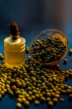 Shot of a bowl of green peas along with its extracted oil in a glass bottle on a black surface.