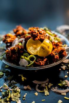 Indian styled meatballs or kabab or kebab on glass plate along with sprinkled cut green chilies and onion rings plus lemon.