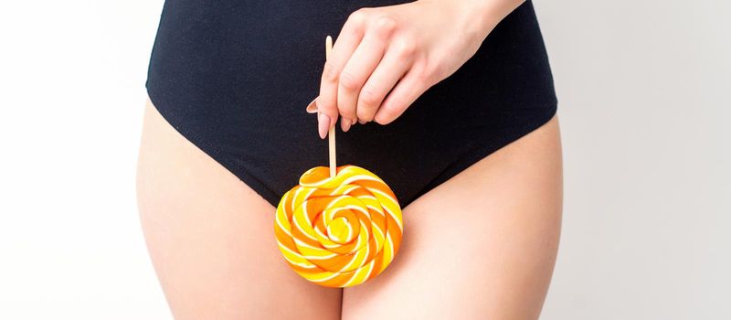 Woman holding lollipop candy on bikini zone, the concept of intimate depilation, problems of intimate hygiene