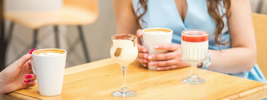 Hands of a young woman holding a cup of coffee with different cocktails on the table at the cafe