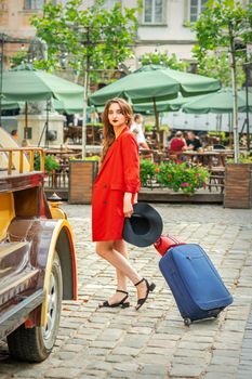 Tourist business young woman in beautiful red jacket is pulling the suitcase on the city street