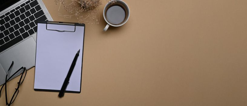 Overhead view laptop computer, clipboard and coffee cup on beige background.