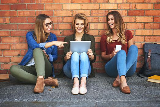 Enjoying the free campus wifi. three smiling female university students sitting together outside on campus using a digital tablet