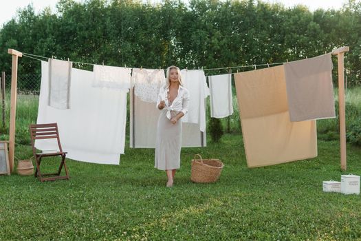 Laundry day. A woman hangs linen and towels on a tree in the courtyard of a village house. Summer cottage concept.