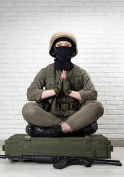 girl soldier in a helmet sits in the lotus position on a box of ammunition