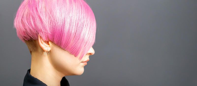 Profile portrait of a young caucasian woman with pink bob haircut isolated on a gray background, copy space