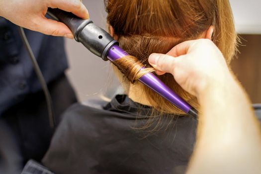 Close up of hairstylist's hands using a curling iron for hair curls in a beauty salon