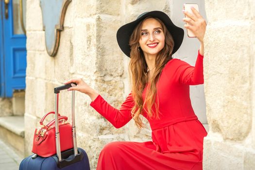 Beautiful young caucasian woman in black hat looking on the smartphone smiling and sitting on stairs at the door outdoors