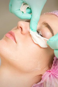 Young woman receiving eyelash removal procedure and removes mascara with a cotton swab and stick in a beauty salon