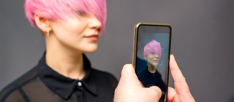 Man hairdresser's hands taking picture on smartphone of her client short pink hairstyle
