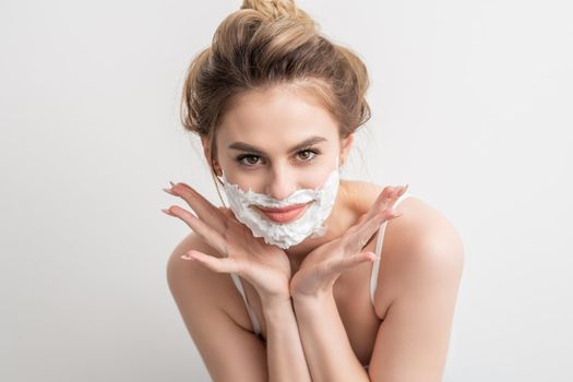 Portrait of a beautiful young smiling caucasian woman with shaving foam on face poses on white background