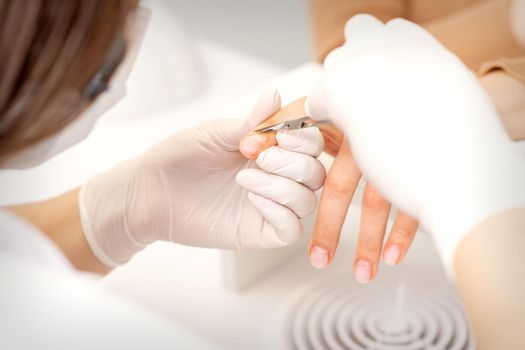Close up of manicure master with manicure scissors removes cuticles of female nails at beauty salon
