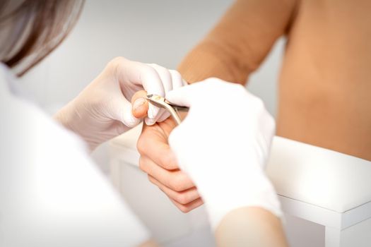 Close up of manicure master with manicure nipper cuts cuticles of female nails at beauty salon