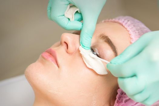 Young woman receiving eyelash removal procedure and removes mascara with a cotton swab and stick in a beauty salon