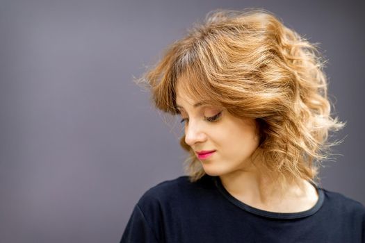 Beautiful young caucasian woman with a red short curly hairstyle looking down on dark background