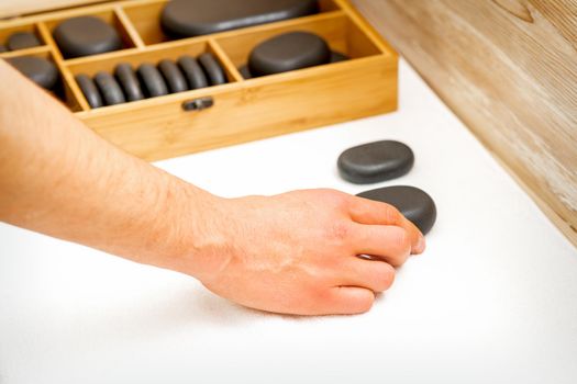 Hand of masseur takes black massage stones from the table in spa salon