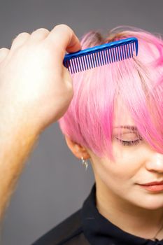 Professional hairdresser checks hairstyle with a comb of young beautiful caucasian woman