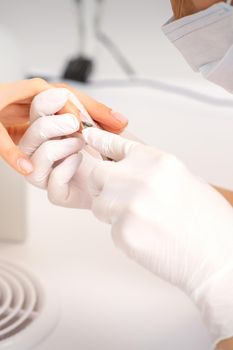 Close up of manicure master with manicure nipper cuts cuticles of female nails at beauty salon