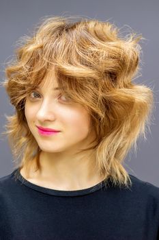 Beautiful young caucasian woman with a red short curly hairstyle on dark background