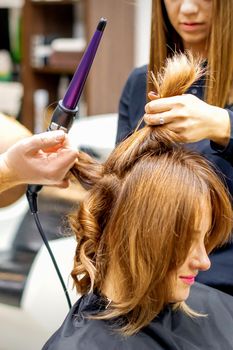 Two hairstylists using curling iron on customers long brown hair in a beauty salon