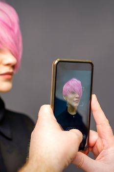 Man hairdresser's hands taking picture on smartphone of her client short pink hairstyle