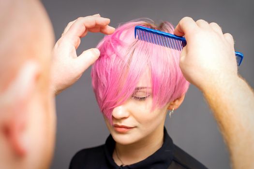 Professional hairdresser checks hairstyle with a comb of young beautiful caucasian woman