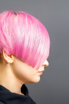 Profile portrait of a young caucasian woman with pink bob haircut isolated on a gray background