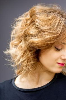 Beautiful young caucasian woman with a red short curly hairstyle looking down on dark background