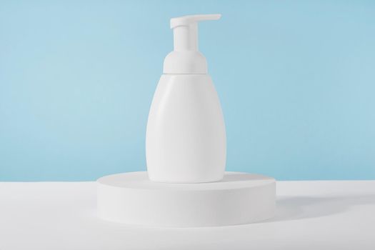 Bath soap white cosmetic bottle mockup on white podium pedestal on blue background. Body care foam product or lotion packaging. Plastic cosmetics tube front view mock up. Body hygiene cream