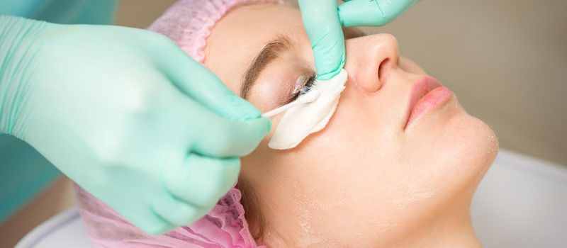 Young woman receiving eyelash removal procedure and removes mascara with a cotton swab and stick in a beauty salon