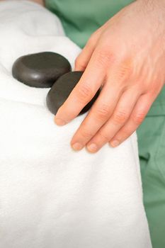 Close up of masseur's hand wipes black massage stones with a white towel