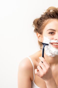 Portrait of beautiful young smiling caucasian woman shaves face with razor on white background