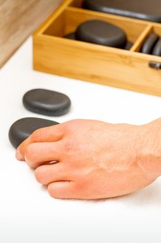 Hand of masseur takes black massage stones from the table in spa salon