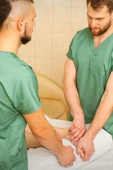 Two masseurs do foot massage in four hands for a female client in a spa salon