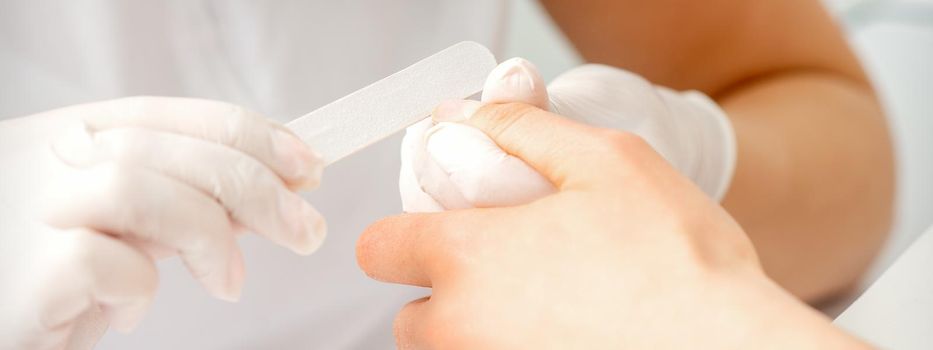 Close up of the hand of young woman receiving the nail file procedure in a beauty salon