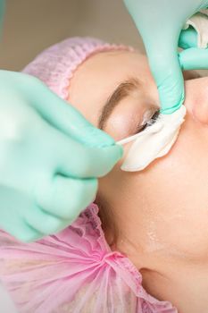 Young woman receiving eyelash removal procedure and removes mascara with a cotton swab and stick in a beauty salon
