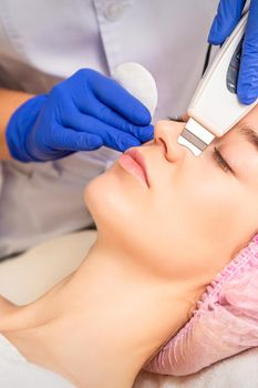 Closeup of beautiful young woman receiving ultrasound facial exfoliation and cavitation facial peeling with ultrasonic equipment in cosmetology office