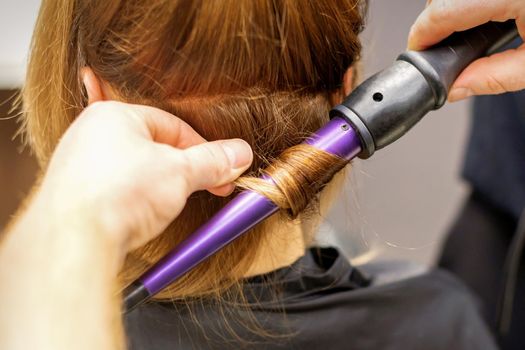 Close up of hairstylist's hands using a curling iron for hair curls in a beauty salon