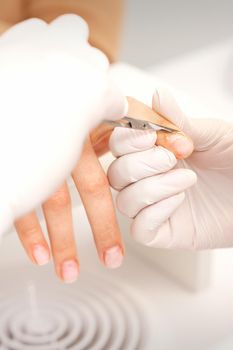 Close up of manicure master with manicure scissors removes cuticles of female nails at beauty salon