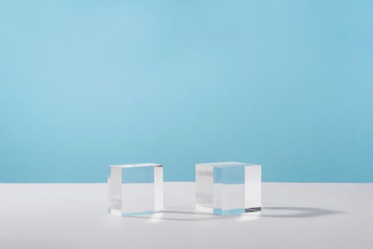 Pedestal cosmetic display glass podium platform with stylish props for product presentation, cosmetics geometric stand, mockup scene for jewellery. Acrylic blocks cubeson blue background