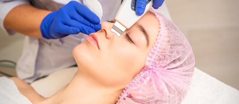 Closeup of beautiful young woman receiving ultrasound facial exfoliation and cavitation facial peeling with ultrasonic equipment in cosmetology office