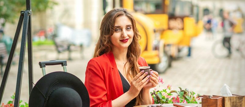 Tourist young caucasian woman in red jacket with coffee cup at the table in cafe outdoors