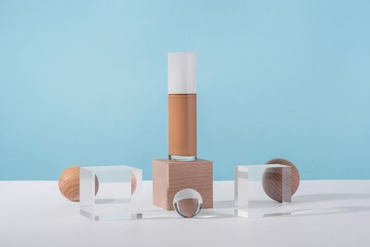 Cosmetic liquid foundation nude cream bottle mockup on acrylic and wooden block podium pedestal. Beige concealer base cosmetics product mock up on blue backdrop. Skincare beauty primer, bb corrector