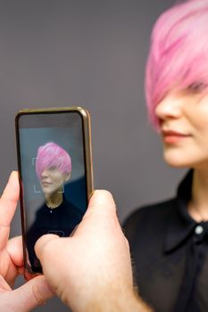 Man hairdresser's hands taking picture on smartphone of her client short pink hairstyle