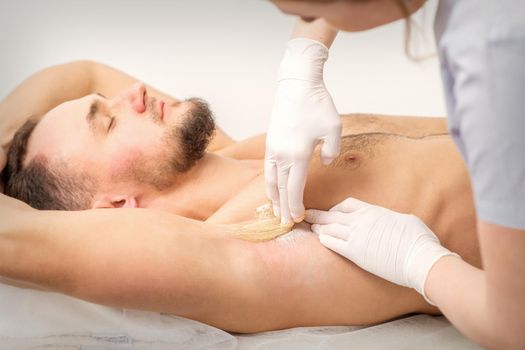 Young caucasian man receiving hair removal from his armpit in a beauty salon, depilation men's underarm