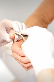 Close up of manicure master with manicure nipper cuts cuticles of female nails at beauty salon