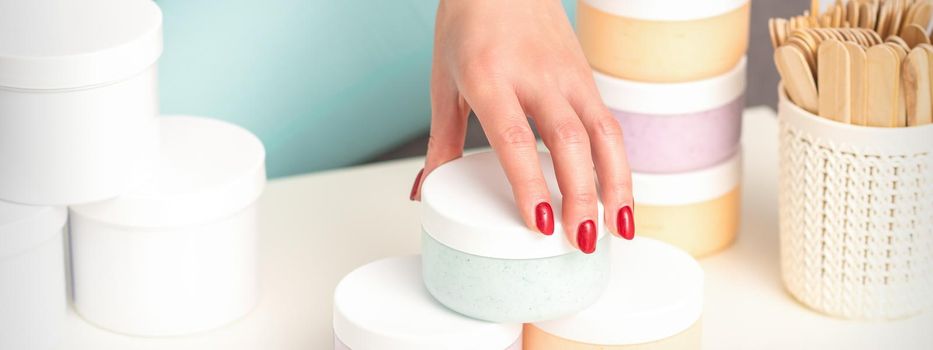 Beautician's hand takes jar with cosmetics from table offering and selling cosmetic products, moisturizing cream, wax paste