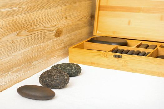 Black massage stones lying near the wooden box with massage rocks on the towel on the table