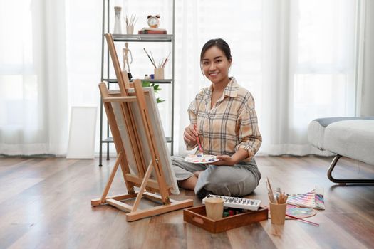 Joyful young female artist painting on canvas at workshop.