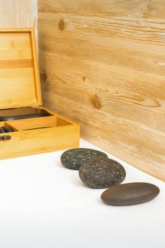 Black massage stones lying near the wooden box with massage rocks on the towel on the table